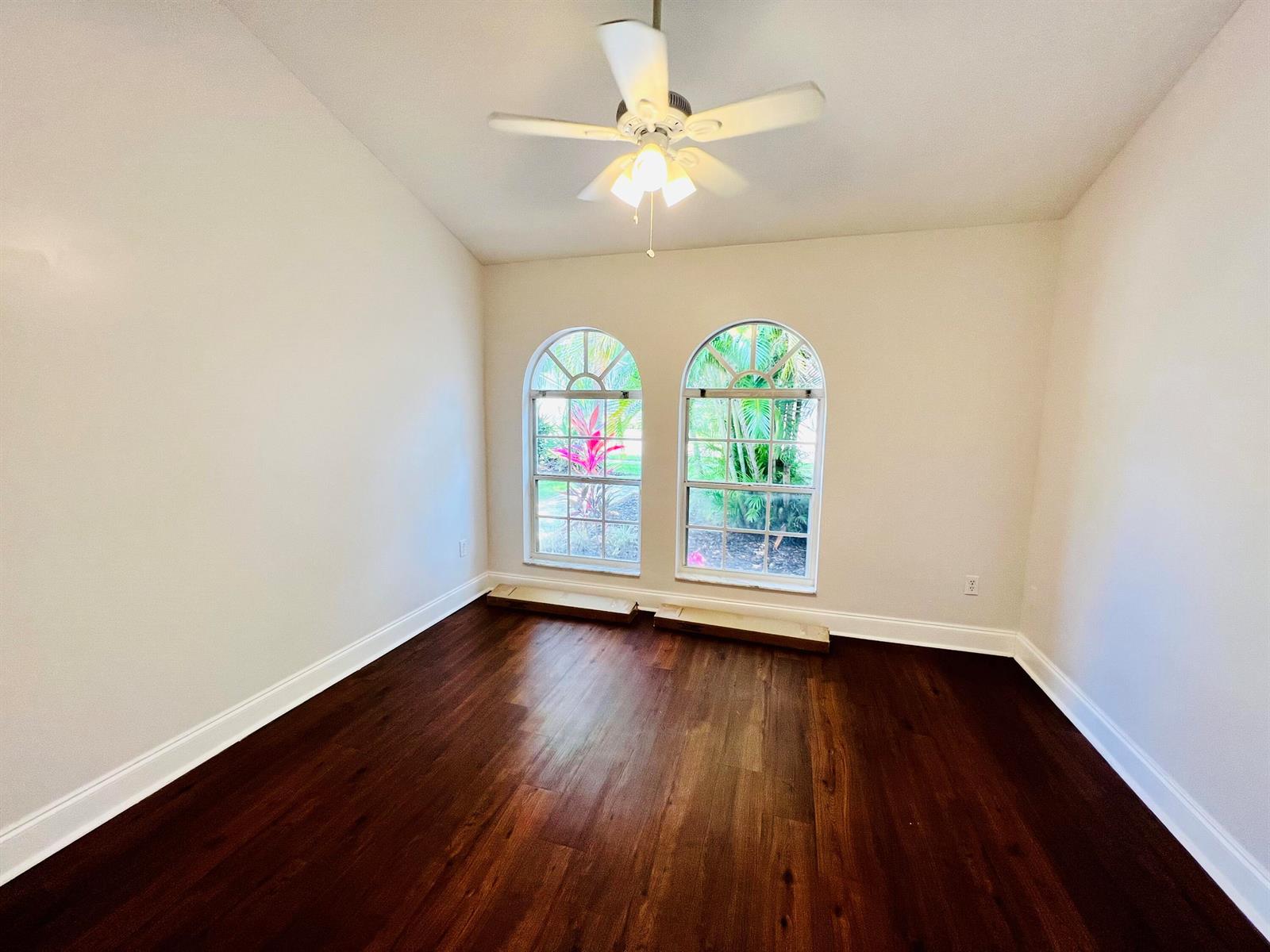An empty room with dark hardwood floors, white walls, and two arched windows — 2485 Stonegate Drive, Wellington FL 33414, WELLINGTON, FL