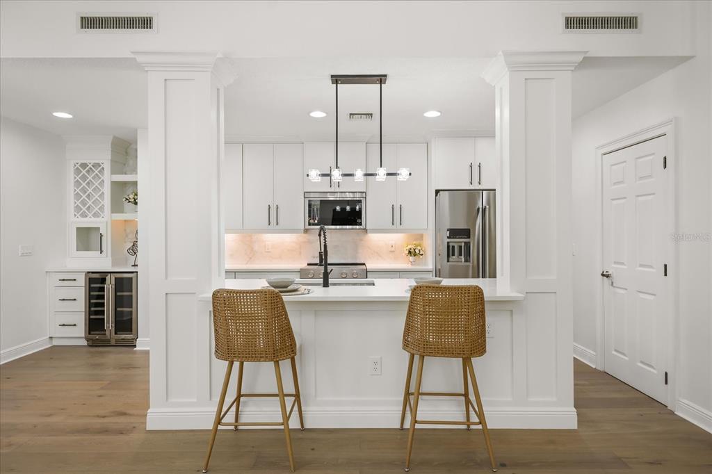 A modern white kitchen features a breakfast bar with two woven stools and pendant lighting — 1567 LAKE BALDWIN LANE, ORLANDO, FL