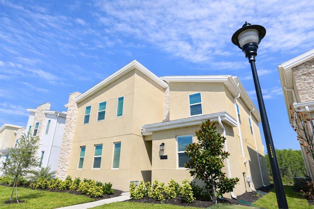 A two-story beige stucco house with stone accents stands under a bright blue sky — 2956 PENELOPE LOOP, KISSIMMEE, FL