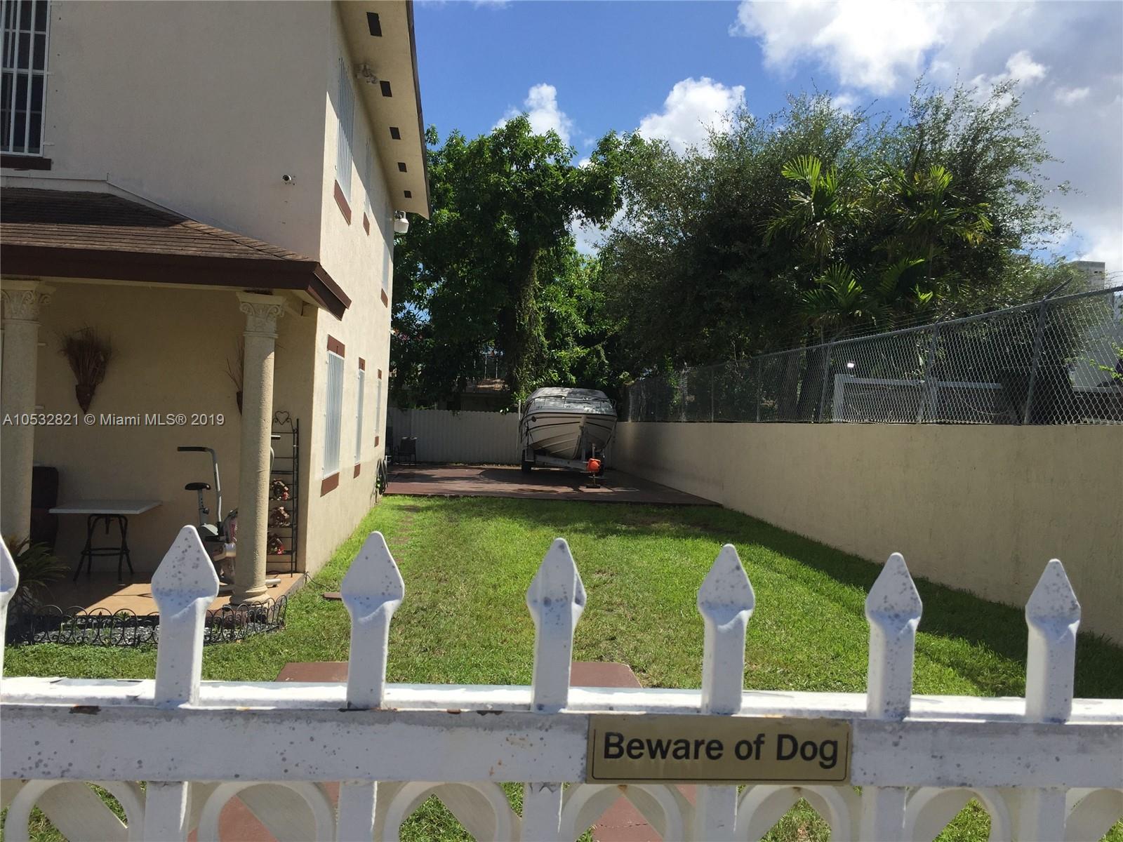 A white fence with a warning sign stands before a grassy yard and a boat — 160 NW 27th St, Miami FL 33127, MIAMI, FL
