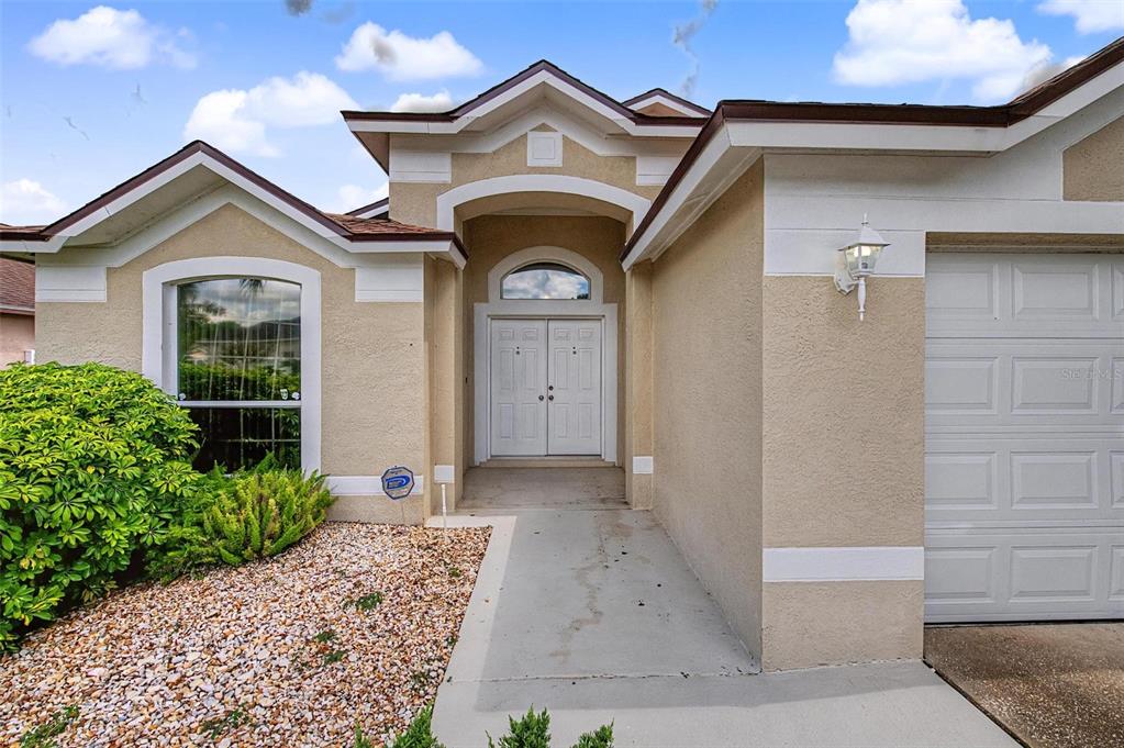 The exterior of a tan stucco house features a double front door and garage — 29641 FOG HOLLOW DRIVE, WESLEY CHAPEL, FL