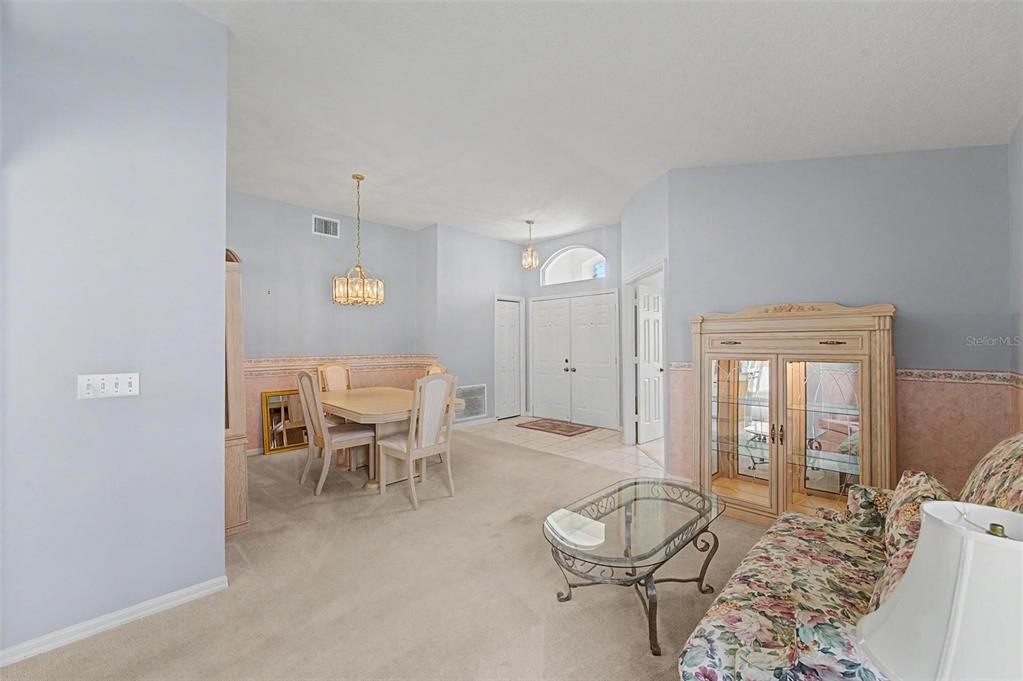A dining area and living space feature light blue walls, beige carpet, and floral furniture — 29641 FOG HOLLOW DRIVE, WESLEY CHAPEL, FL