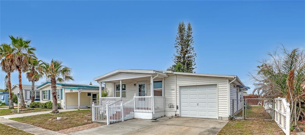 A white single-story manufactured home features a front porch, a garage, and palm trees — 1818 BIG CYPRESS STREET NE, PALM BAY, FL