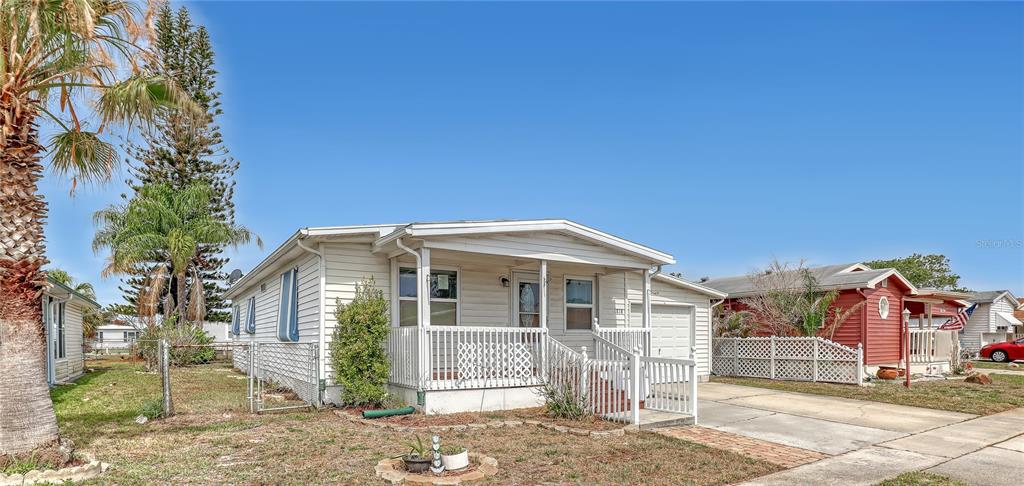 A white mobile home with a front porch sits on a grassy lot next to a red house — 1818 BIG CYPRESS STREET NE, PALM BAY, FL