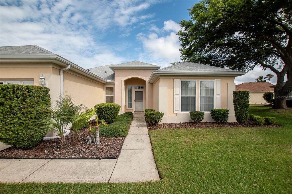 A single-story house with a beige stucco exterior, a front walkway, and manicured landscaping — 13126 SE 93RD TERRACE ROAD, SUMMERFIELD, FL