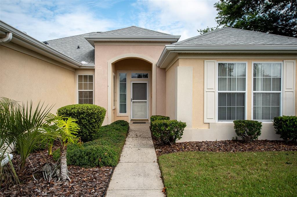 The exterior of a single-story house features a concrete walkway leading to a recessed entryway — 13126 SE 93RD TERRACE ROAD, SUMMERFIELD, FL