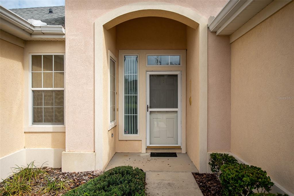 The exterior view shows a beige stucco home entrance with a white storm door — 13126 SE 93RD TERRACE ROAD, SUMMERFIELD, FL