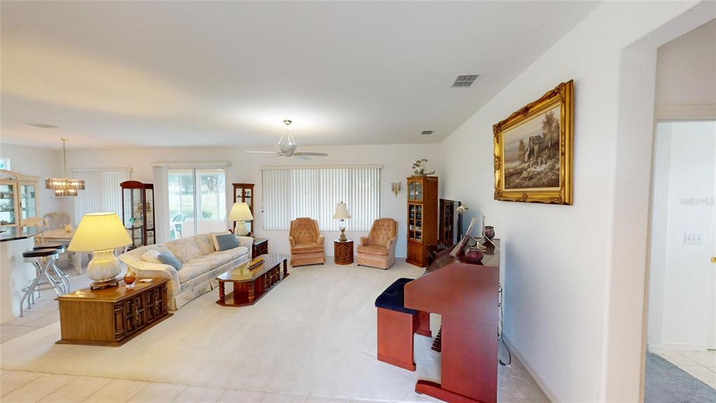 A spacious living room features light carpeting, a sofa, two armchairs, and a piano — 13126 SE 93RD TERRACE ROAD, SUMMERFIELD, FL