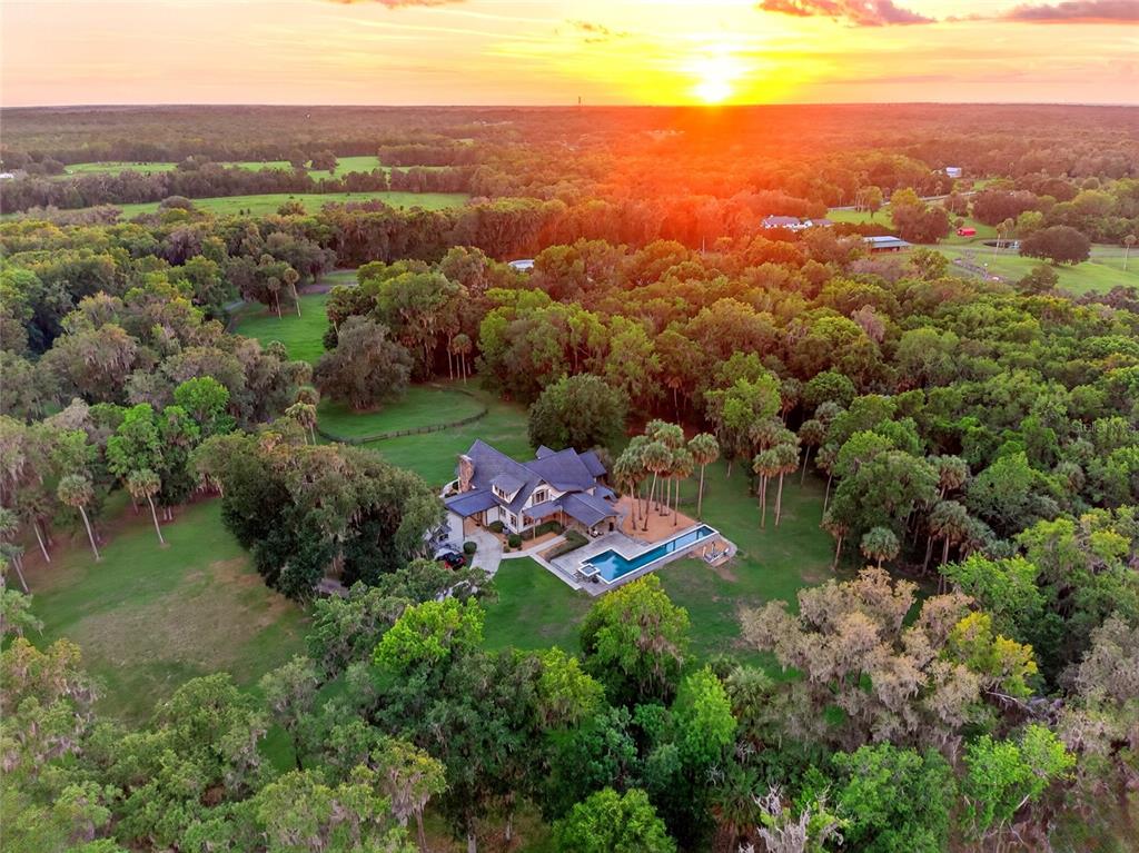 An aerial view shows a house with a swimming pool surrounded by trees at sunset — 7000 NW HWY 320, MICANOPY, FL