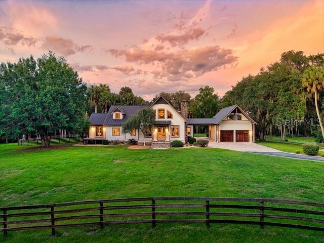 A two-story house with a detached garage sits on a grassy lot at sunset — 7000 NW HWY 320, MICANOPY, FL