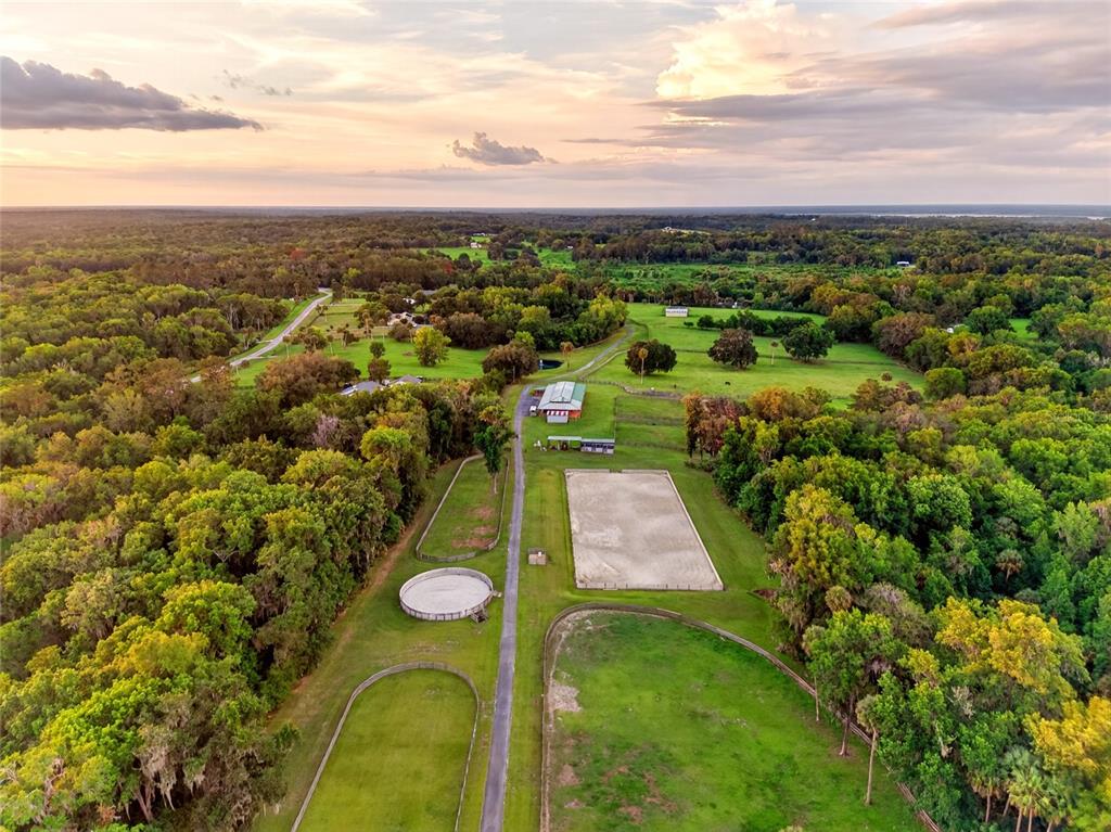 An aerial view shows a rural property with a barn, riding arena, and fenced pastures — 7000 NW HWY 320, MICANOPY, FL