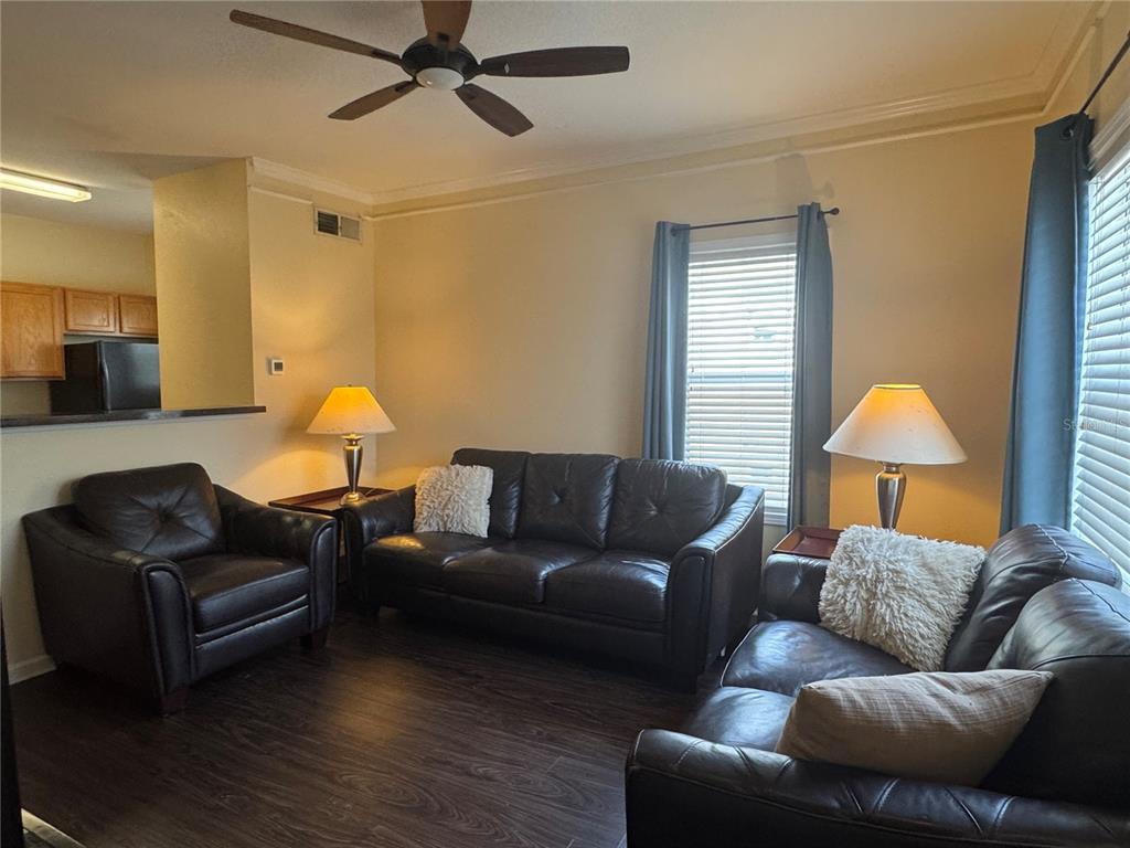 A living room features dark leather furniture, a ceiling fan, and windows with blue curtains — 4802 51ST STREET W UNIT 510, BRADENTON, FL