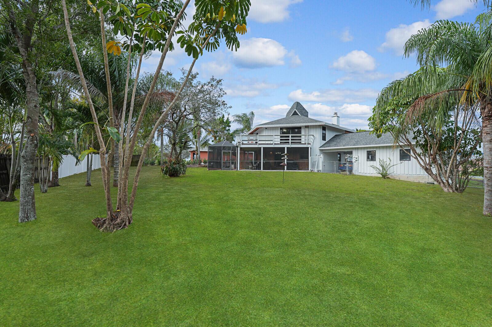 A large backyard with a green lawn leads to a white house with a deck — 9752 SE Highborne Way, Hobe Sound FL 33455, HOBE SOUND, FL
