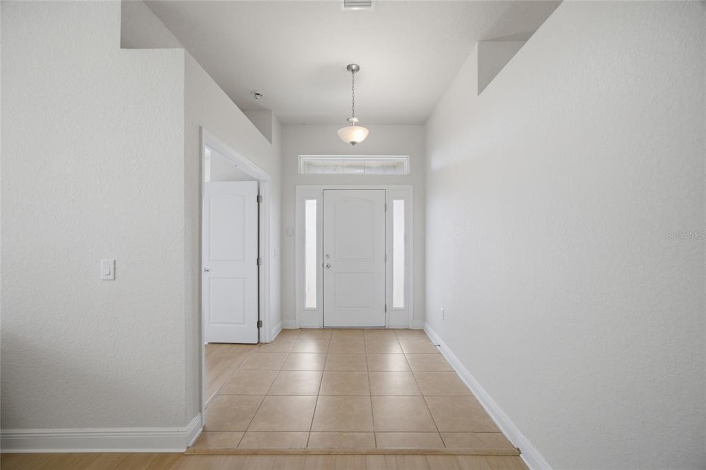 A bright entryway features a white front door, tile flooring, and a hanging light fixture — 3 DIAMOND COVE COURT, OCALA, FL