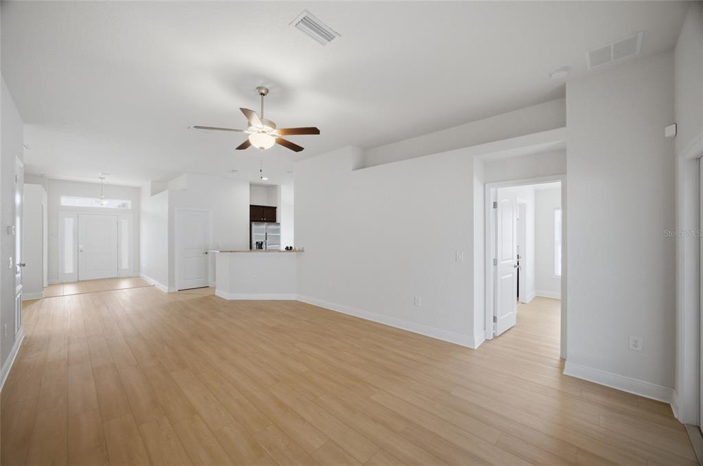 A spacious living room with light wood-look flooring, a ceiling fan, and an open kitchen — 3 DIAMOND COVE COURT, OCALA, FL