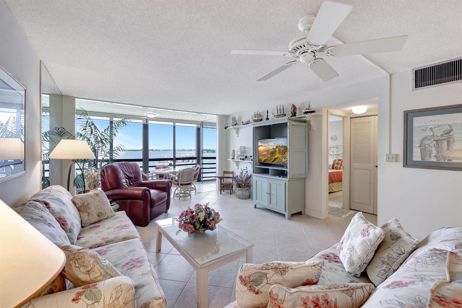 A living room features floral sofas, a red leather chair, and a view of water — 1950 SW Palm City Road # 304, Stuart FL 34994, STUART, FL