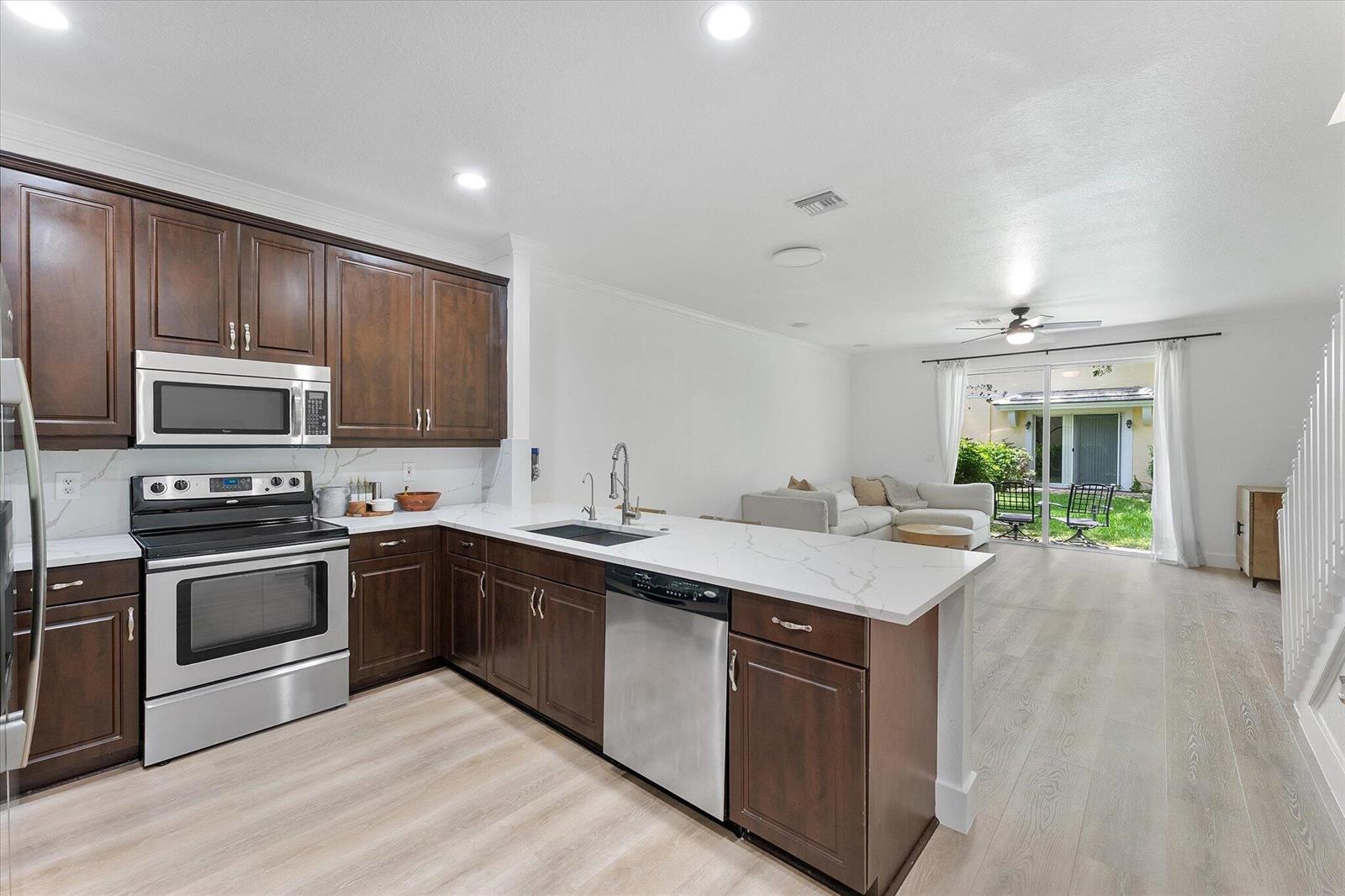 A kitchen with dark wood cabinets and white countertops opens into a living area — 7783 Deercreek Court, Davie FL 33328, DAVIE, FL