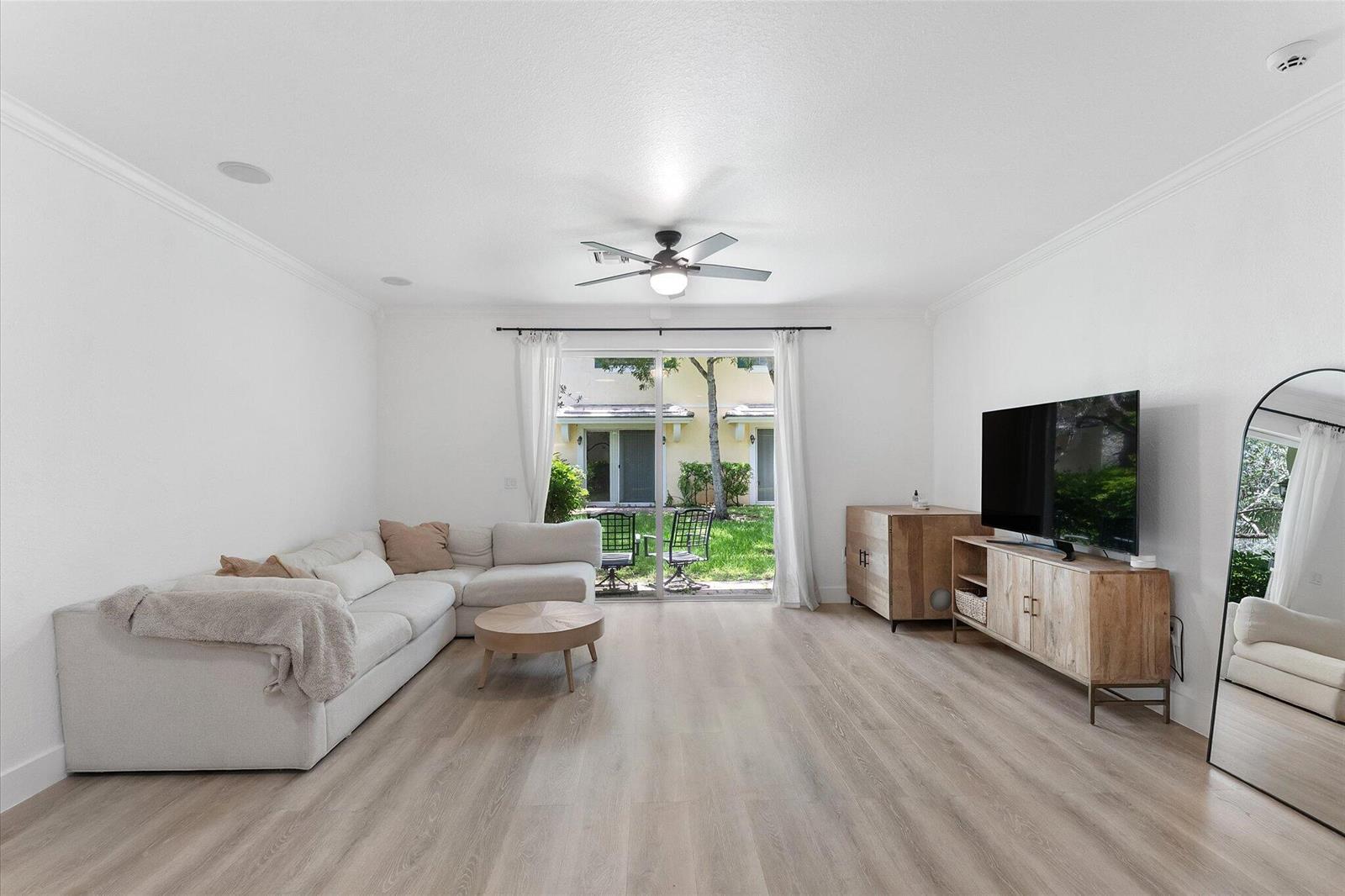 A living room features a white sectional sofa, wood media console, and sliding glass doors — 7783 Deercreek Court, Davie FL 33328, DAVIE, FL