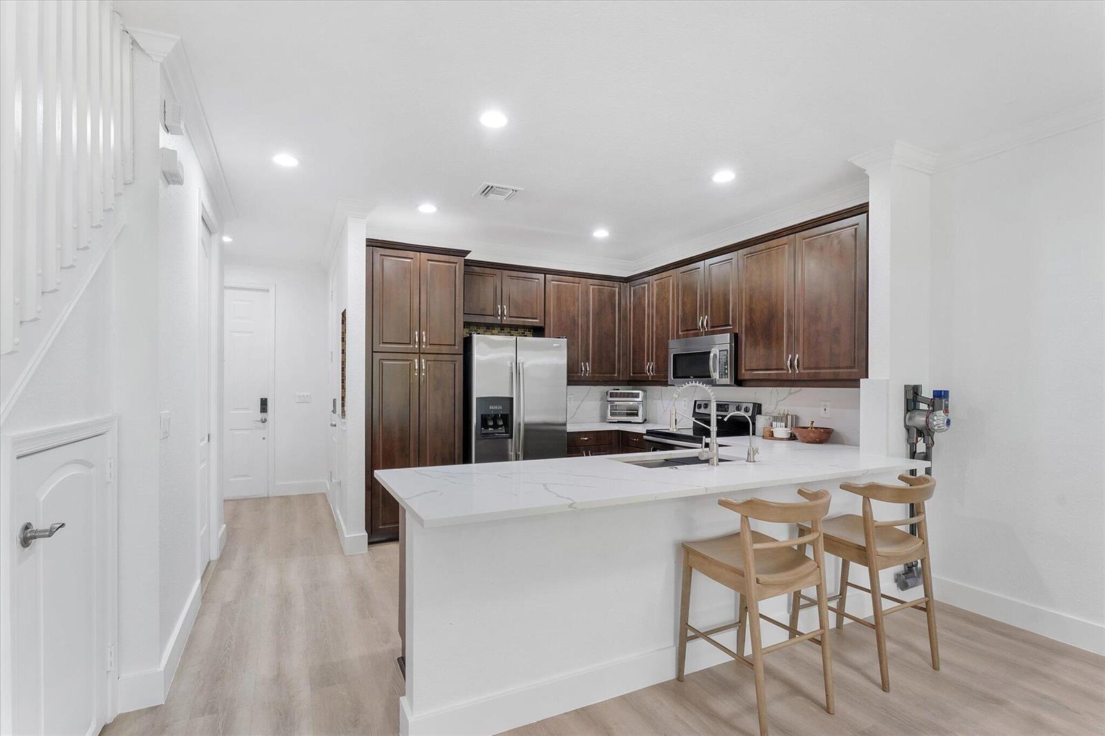 A kitchen with dark wood cabinets, white countertops, and two wooden bar stools — 7783 Deercreek Court, Davie FL 33328, DAVIE, FL