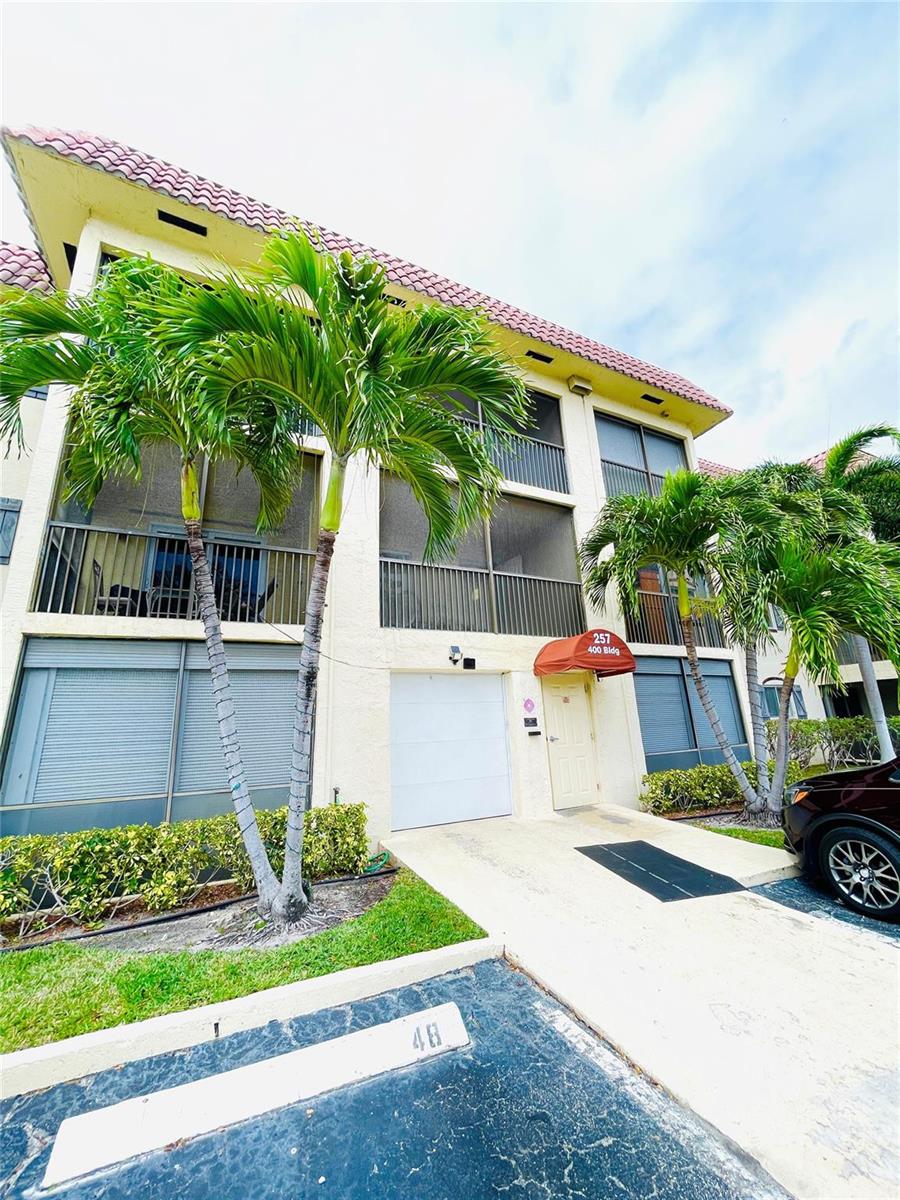 A three-story building exterior features a white garage door, a red awning, and palm trees — 257 S Cypress Road # 414, Pompano Beach FL 33060, POMPANO BEACH, FL