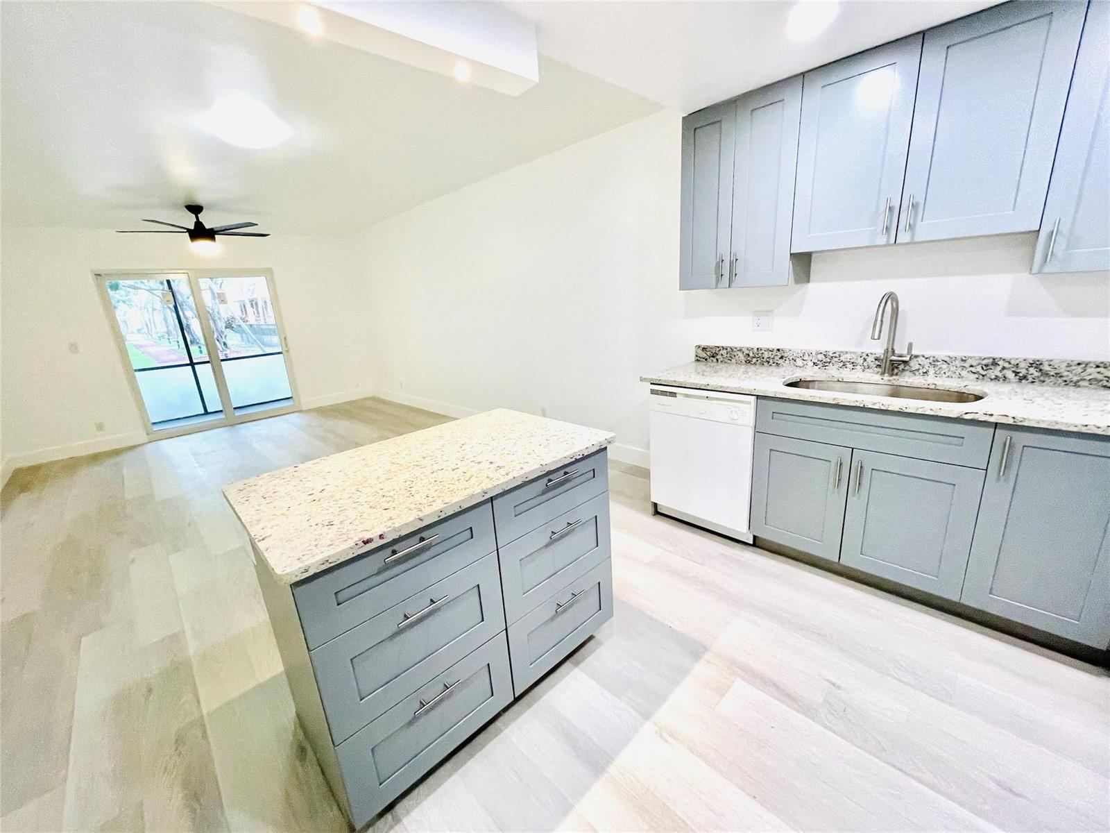 A kitchen with light blue cabinets, granite countertops, and an island opens to a living area — 257 S Cypress Road # 414, Pompano Beach FL 33060, POMPANO BEACH, FL