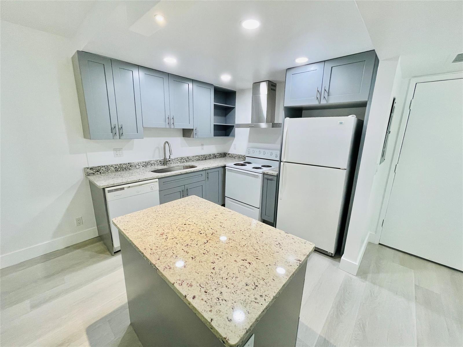 A kitchen features gray cabinets, granite countertops, a kitchen island, and white appliances — 257 S Cypress Road # 414, Pompano Beach FL 33060, POMPANO BEACH, FL