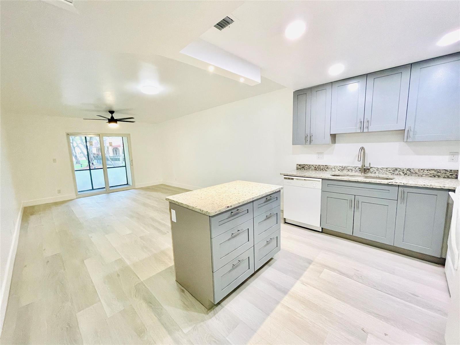 A kitchen with gray cabinets and a granite island opens into a living area — 257 S Cypress Road # 414, Pompano Beach FL 33060, POMPANO BEACH, FL