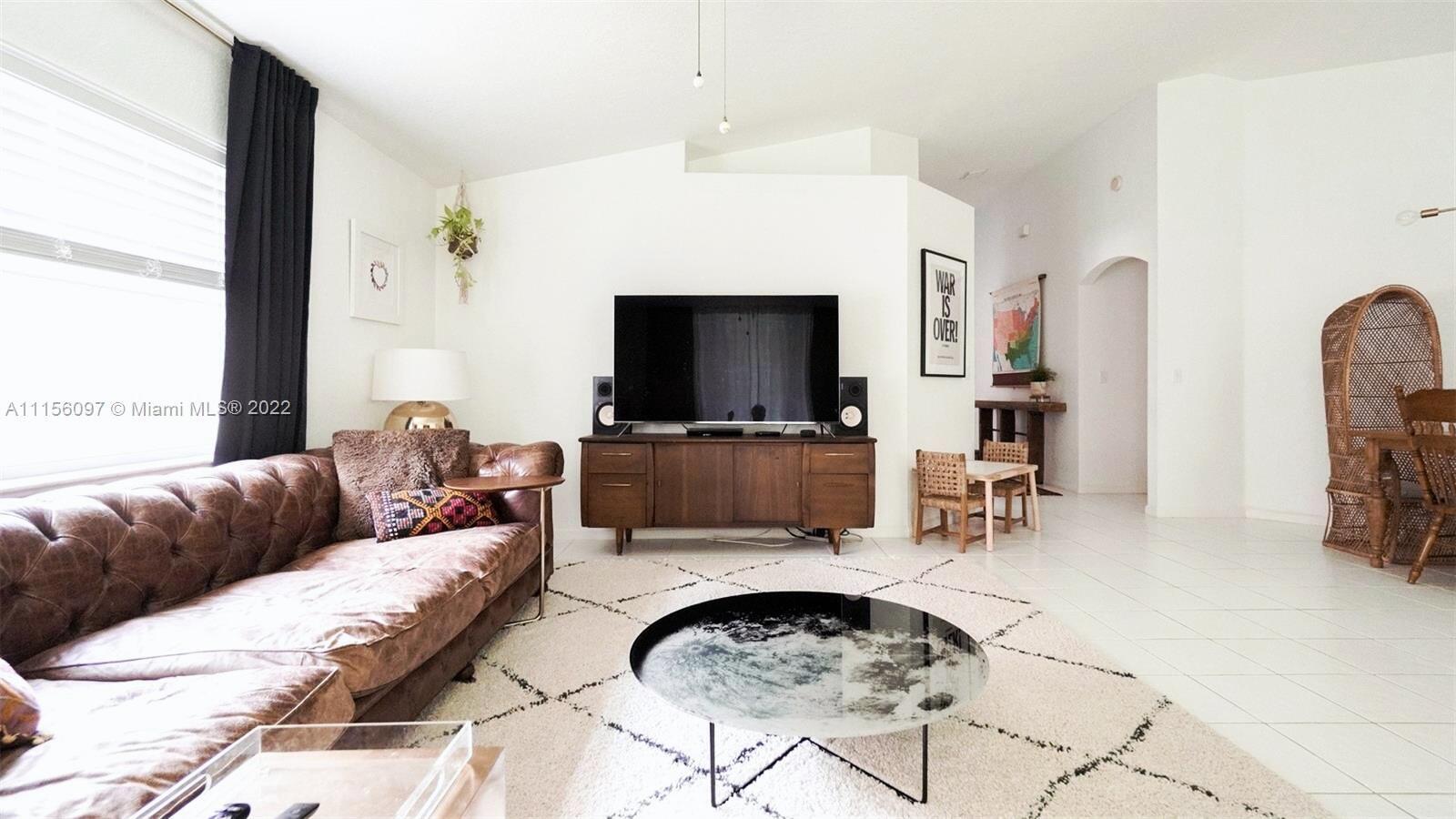 A living room features a brown leather sofa, a round coffee table, and a television — 5449 Grande Palm Circle, Delray Beach FL 33484, DELRAY BEACH, FL