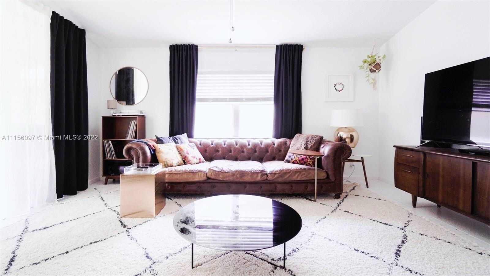 A living room features a brown leather tufted sofa, a round coffee table, and curtains — 5449 Grande Palm Circle, Delray Beach FL 33484, DELRAY BEACH, FL