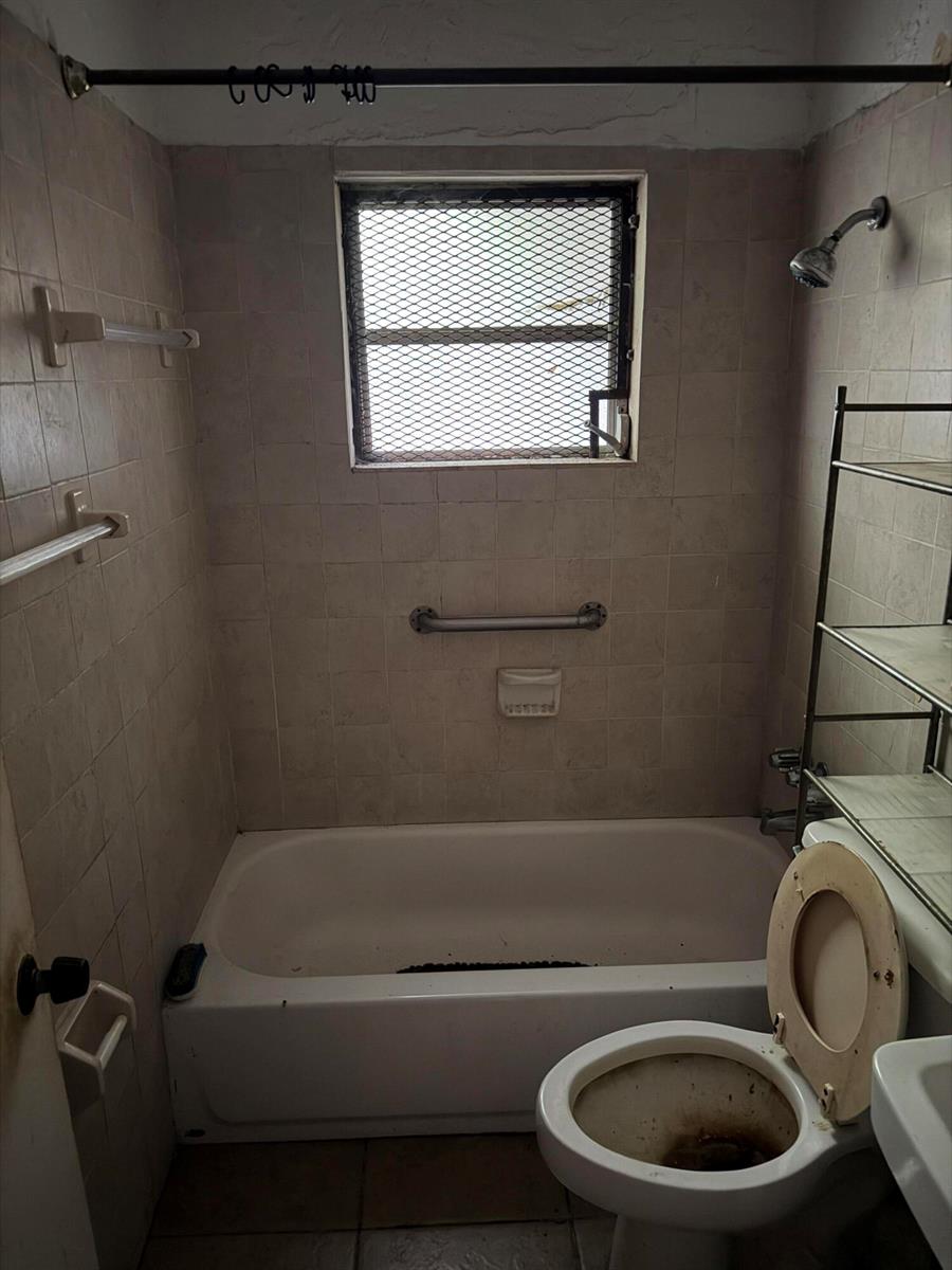 A bathroom features a tiled tub-shower combination, a toilet, and a window with security bars — 1280 NW 51ST Street, Miami FL 33142, MIAMI, FL