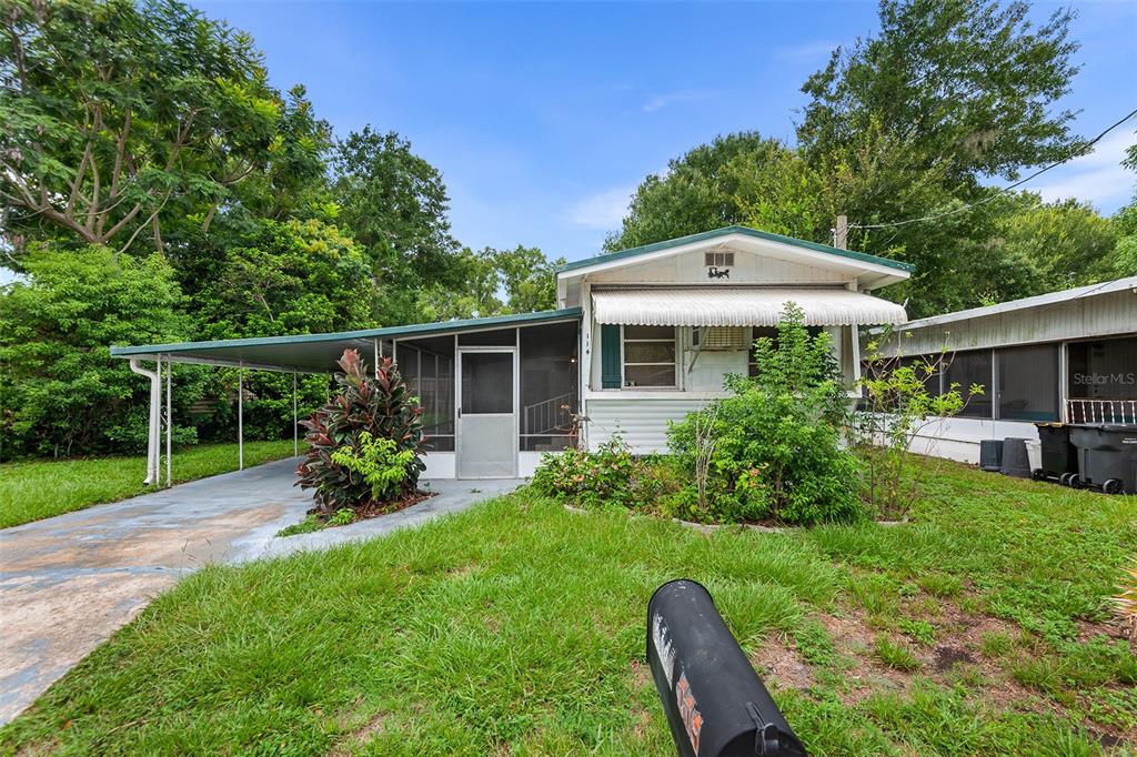A single-story house with a carport, screened porch, and white siding sits on a grassy lot — 114 LAKESIDE DR, AUBURNDALE, FL