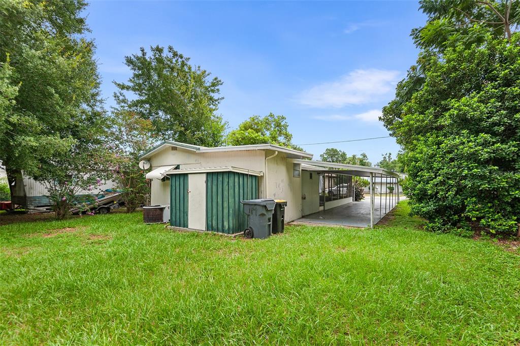 The exterior of a mobile home features a green storage shed, carport, and grassy yard — 114 LAKESIDE DR, AUBURNDALE, FL