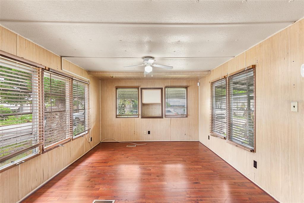 An empty sunroom features wood-paneled walls, wood-look flooring, a ceiling fan, and multiple windows — 114 LAKESIDE DR, AUBURNDALE, FL
