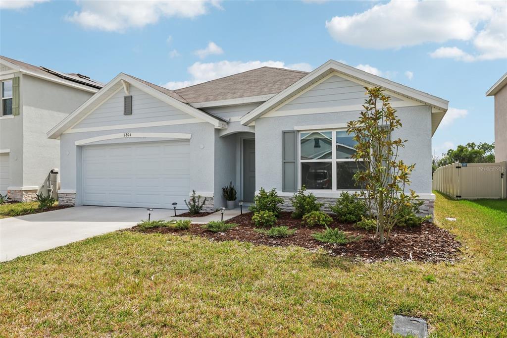 A light blue single-story house with a two-car garage and a landscaped front yard — 1804 TAHITIAN SUNRISE DRIVE, PLANT CITY, FL