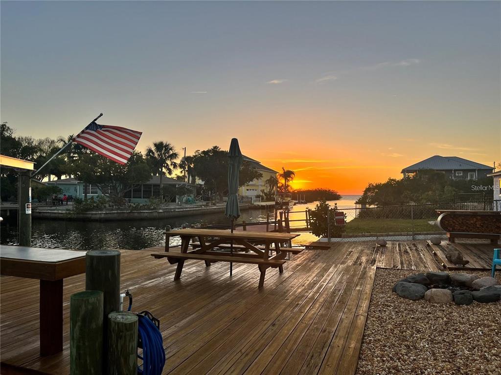 A wooden deck overlooks a canal at sunset with a picnic table and American flag — 6420 BOATYARD DRIVE, HUDSON, FL