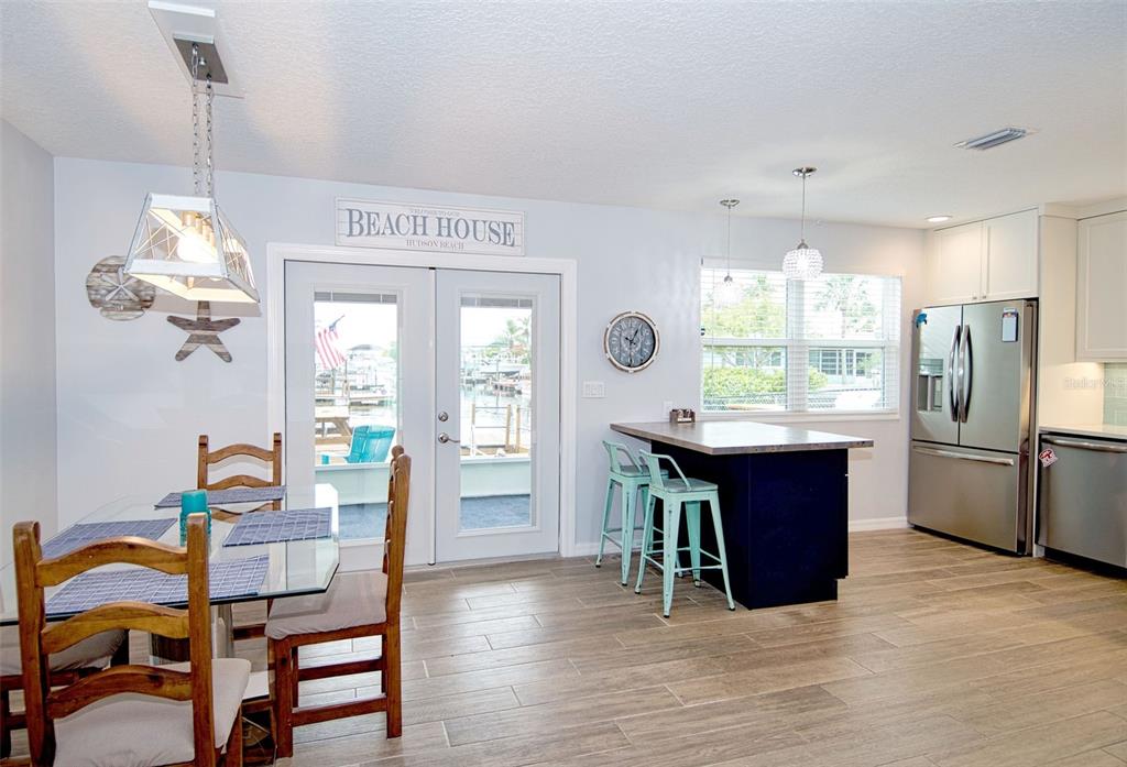 A dining area and kitchen with a glass table, island, and glass doors to a dock — 6420 BOATYARD DRIVE, HUDSON, FL