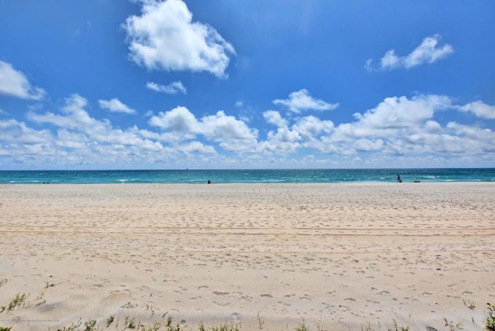 A wide, sandy beach stretches toward the blue ocean under a bright, cloudy sky — 100 Worth Avenue # 7, Palm Beach FL 33480, PALM BEACH, FL