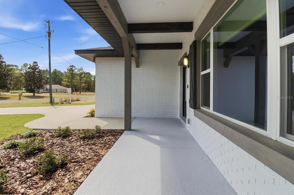A covered front porch with white brick walls, dark wooden beams, and a concrete floor — 7289 N WESTBROOK WAY, CITRUS SPRINGS, FL