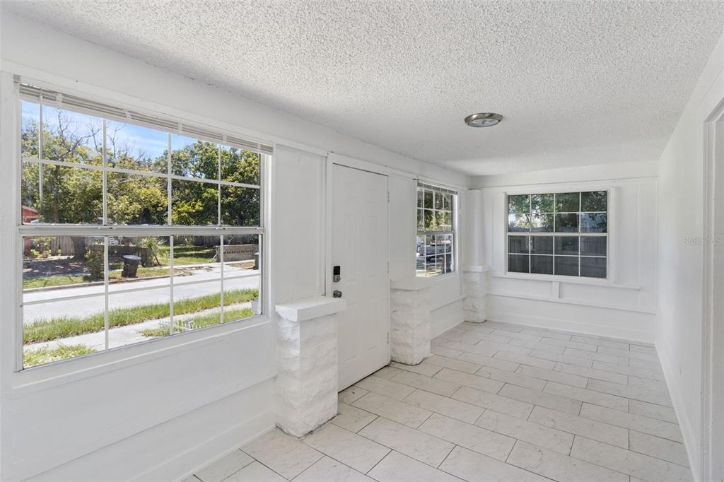 A bright, white-walled sunroom features large windows, a tiled floor, and a central entry door — 1743 YALE STREET S, ST PETERSBURG, FL
