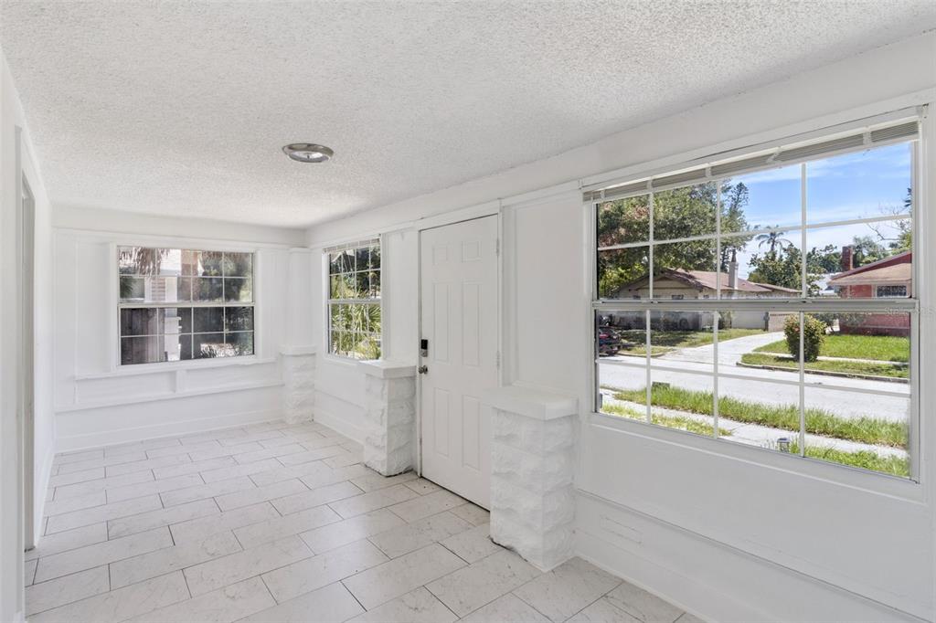 A bright sunroom features white tile flooring, white walls, and large windows overlooking a street — 1743 YALE STREET S, ST PETERSBURG, FL