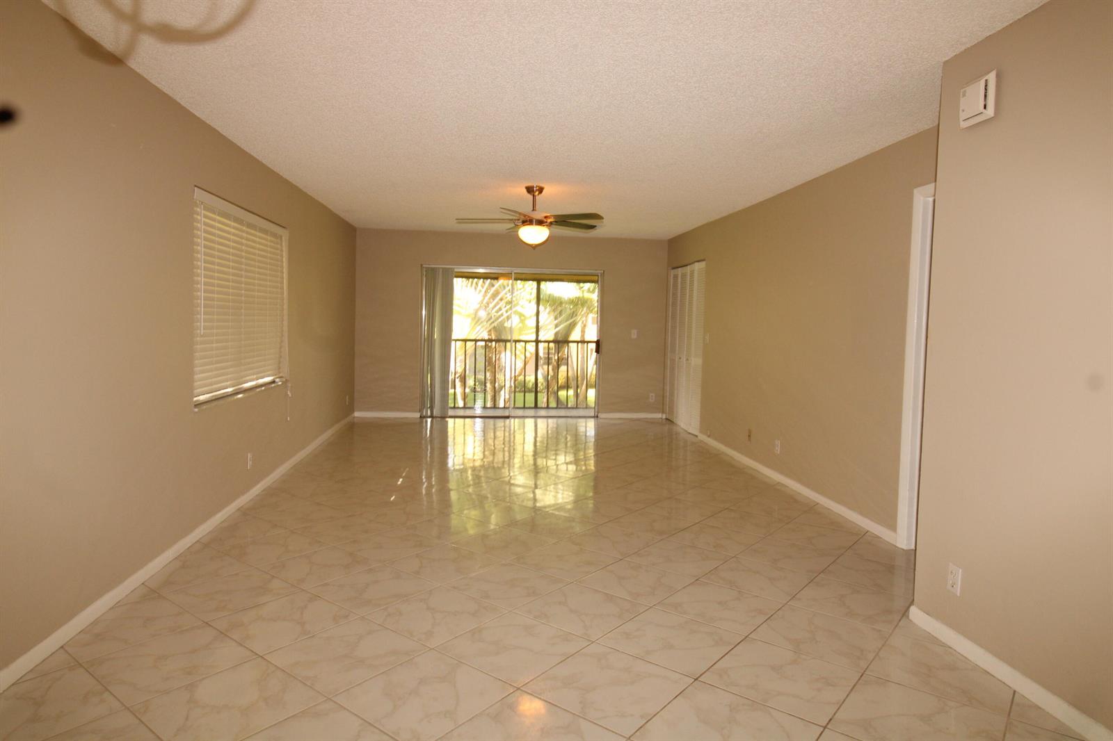 An empty living room features beige walls, light-colored tile flooring, a ceiling fan, and sliding doors — 2955 SW 22nd Avenue # 2080, Delray Beach FL 33445, DELRAY BEACH, FL