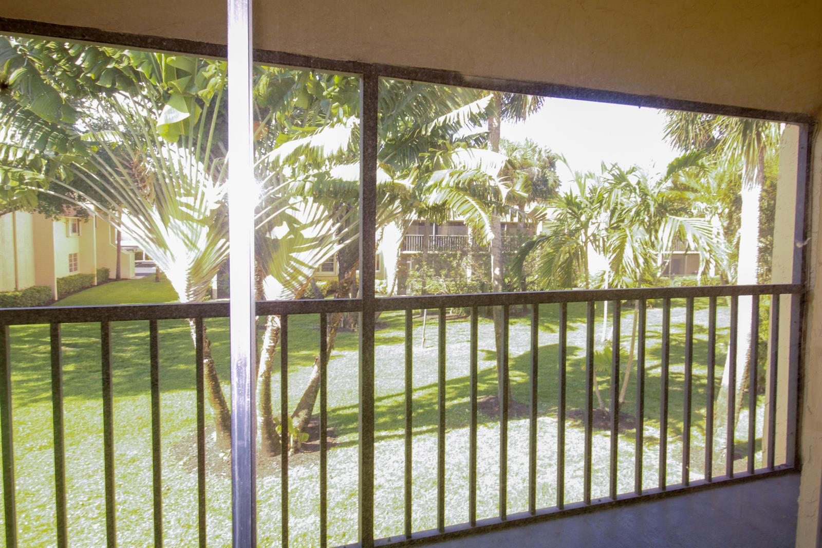 A view of a grassy courtyard with palm trees seen through a screened-in balcony railing — 2955 SW 22nd Avenue # 2080, Delray Beach FL 33445, DELRAY BEACH, FL
