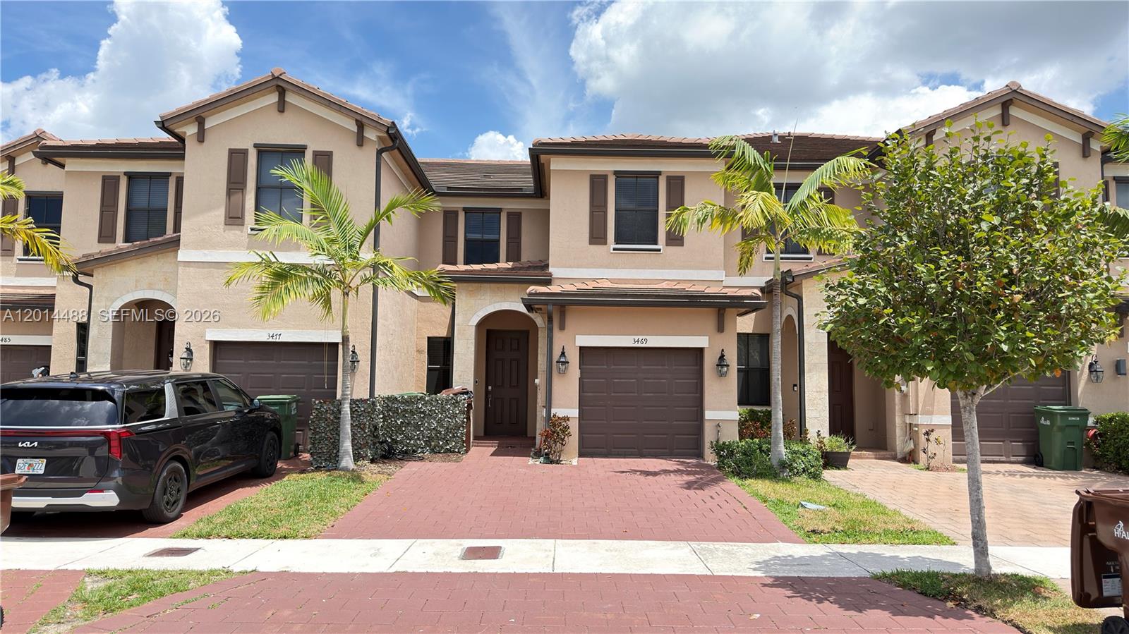 A row of two-story townhouses with tan stucco facades, brown garage doors, and paved driveways — 3469 W 106th St, Hialeah FL 33018, HIALEAH, FL