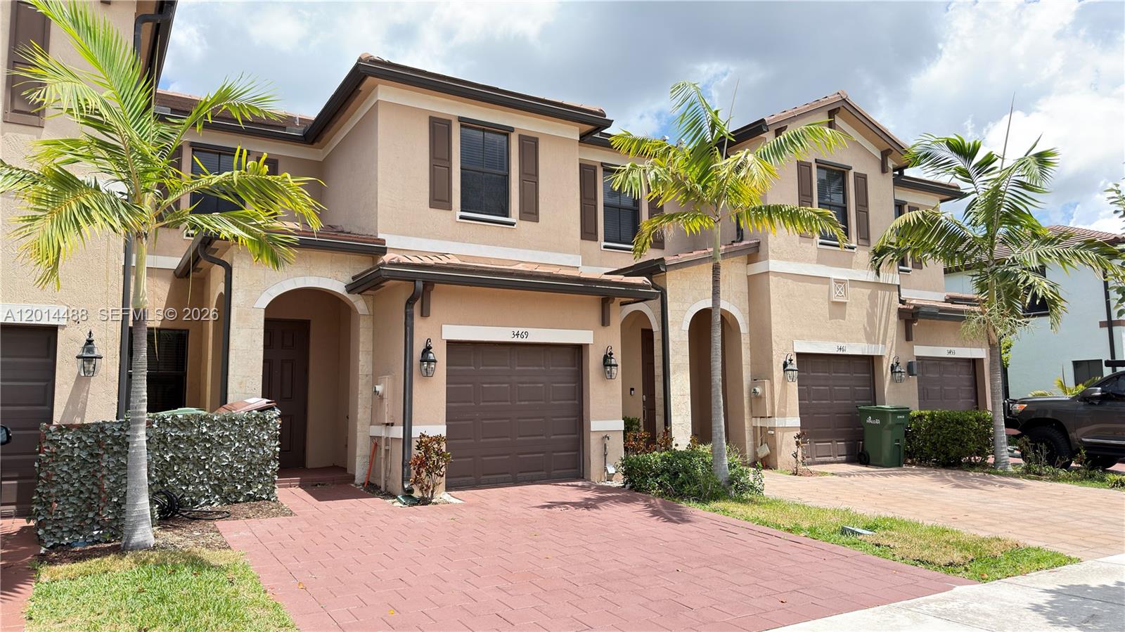 A two-story townhouse exterior features a paved driveway, brown garage doors, and palm trees — 3469 W 106th St, Hialeah FL 33018, HIALEAH, FL
