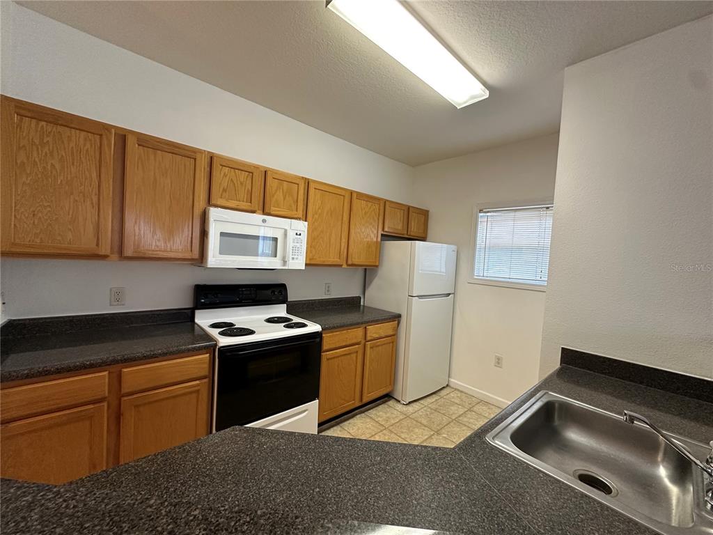 A kitchen features wood cabinets, dark countertops, white appliances, and a stainless steel sink — 4802 51ST STREET W UNIT 622, BRADENTON, FL