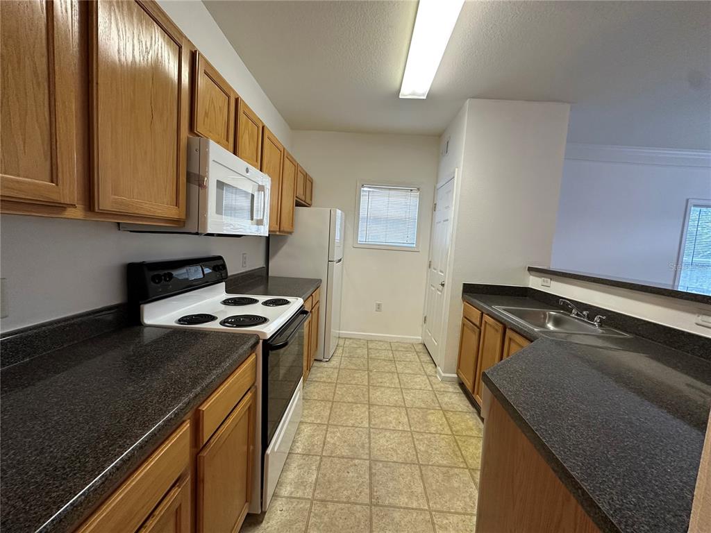 A kitchen features wood cabinets, dark countertops, white appliances, and a tiled floor — 4802 51ST STREET W UNIT 622, BRADENTON, FL