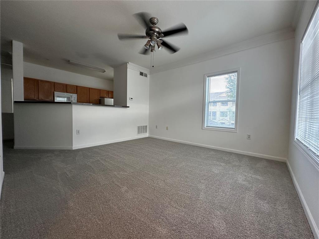 An empty living room with gray carpet, a ceiling fan, and an open kitchen view — 4802 51ST STREET W UNIT 622, BRADENTON, FL