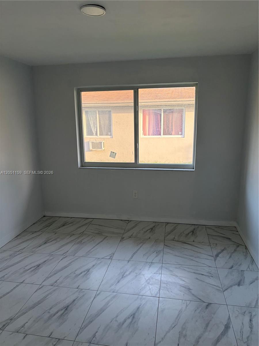 A bedroom features light gray walls, white marble-patterned tile flooring, and a single window — 14399 NE 5th Pl # 3, North Miami FL 33161, NORTH MIAMI, FL
