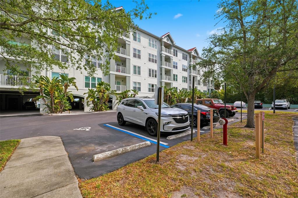 A white multi-story apartment building stands behind a parking lot with several parked cars — 210 3RD STREET W UNIT 8305, BRADENTON, FL
