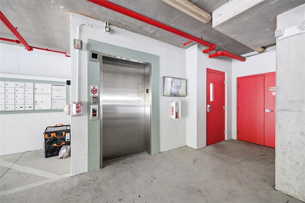 An elevator lobby features a stainless steel elevator, red doors, and a wall of mailboxes — 210 3RD STREET W UNIT 8305, BRADENTON, FL